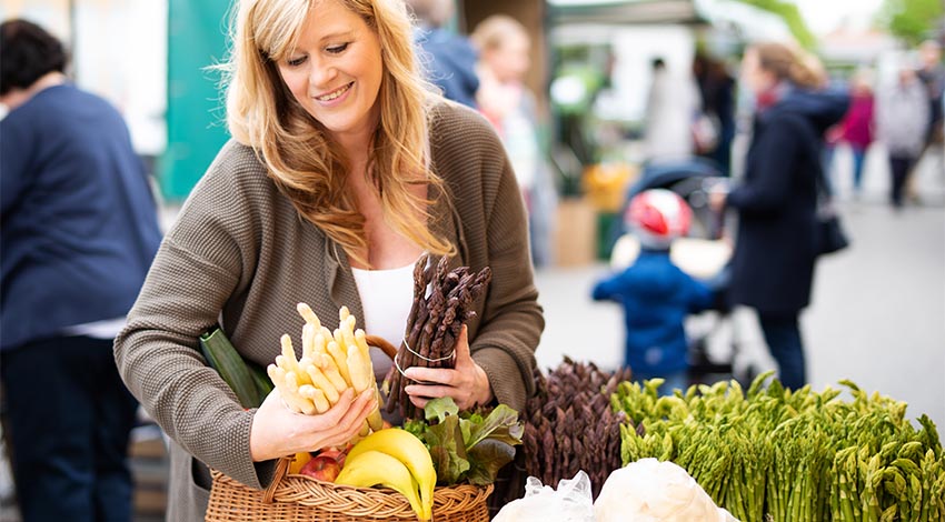 Eine sympathische Frau kauft Spargel auf einem Wochenmarkt ein.